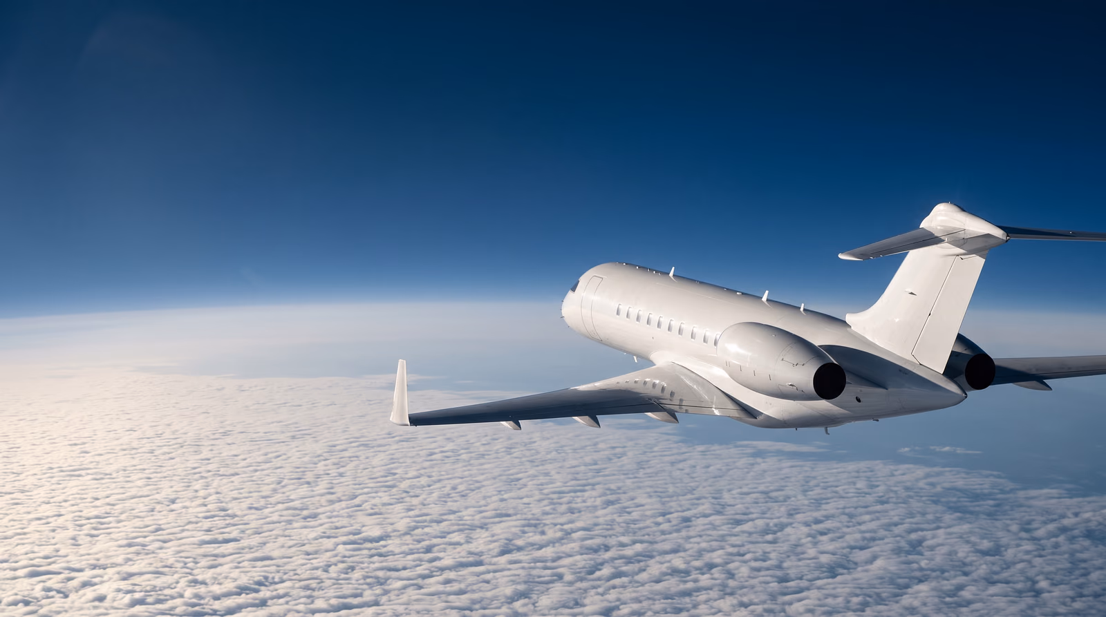 An ultra long range business jet cruising above a solid deck of North Atlantic cloud at high altitude in late afternoon light