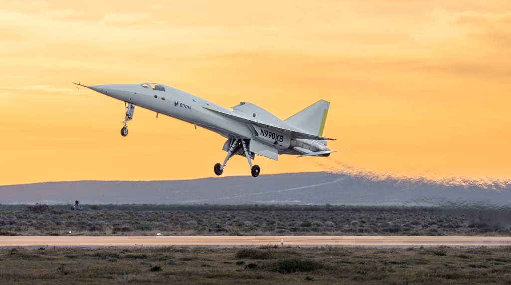 Boom Supersonic Jet aircraft N990XB taking off against a sunset sky, emitting vapor trail. Desert landscape below, mood is dynamic and powerful.