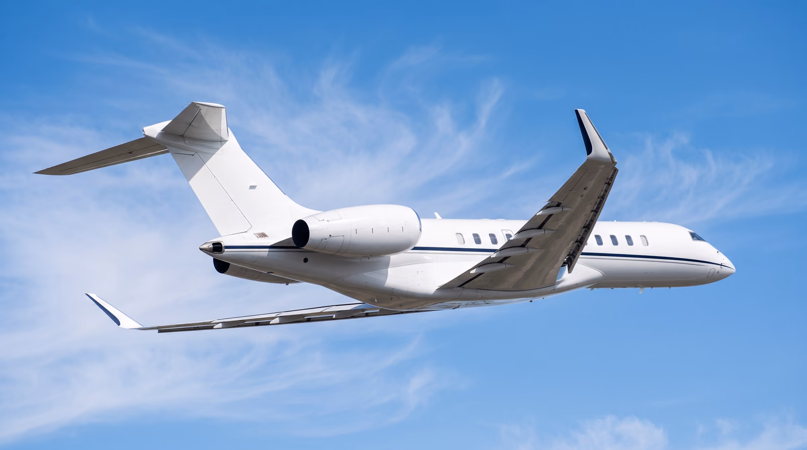 A Bombardier Global series business jet in level cruise flight against a clear blue sky with high cirrus, seen from below and behind with its landing gear retracted.