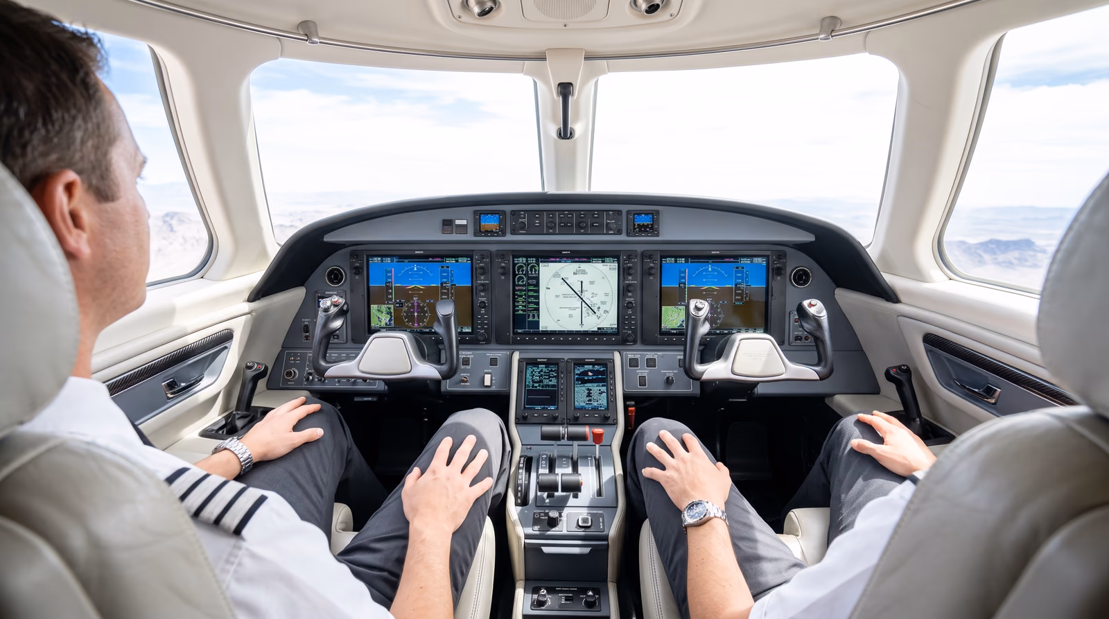 Two pilots sit with their hands resting on their knees, clearly away from the control yokes, in a bright cream and grey business jet cockpit while the glass flight displays show an instrument approach in progress