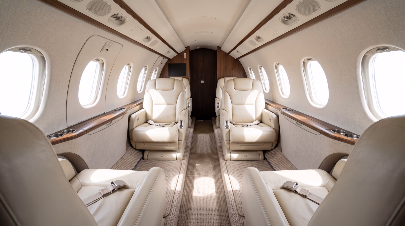 The empty cabin of a midsize business jet, four unoccupied club seats with daylight falling through the oval windows.